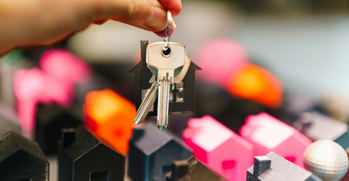 Hand holding house keys over miniature houses