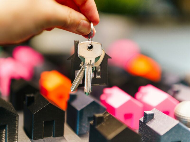 Hand holding house keys over miniature houses