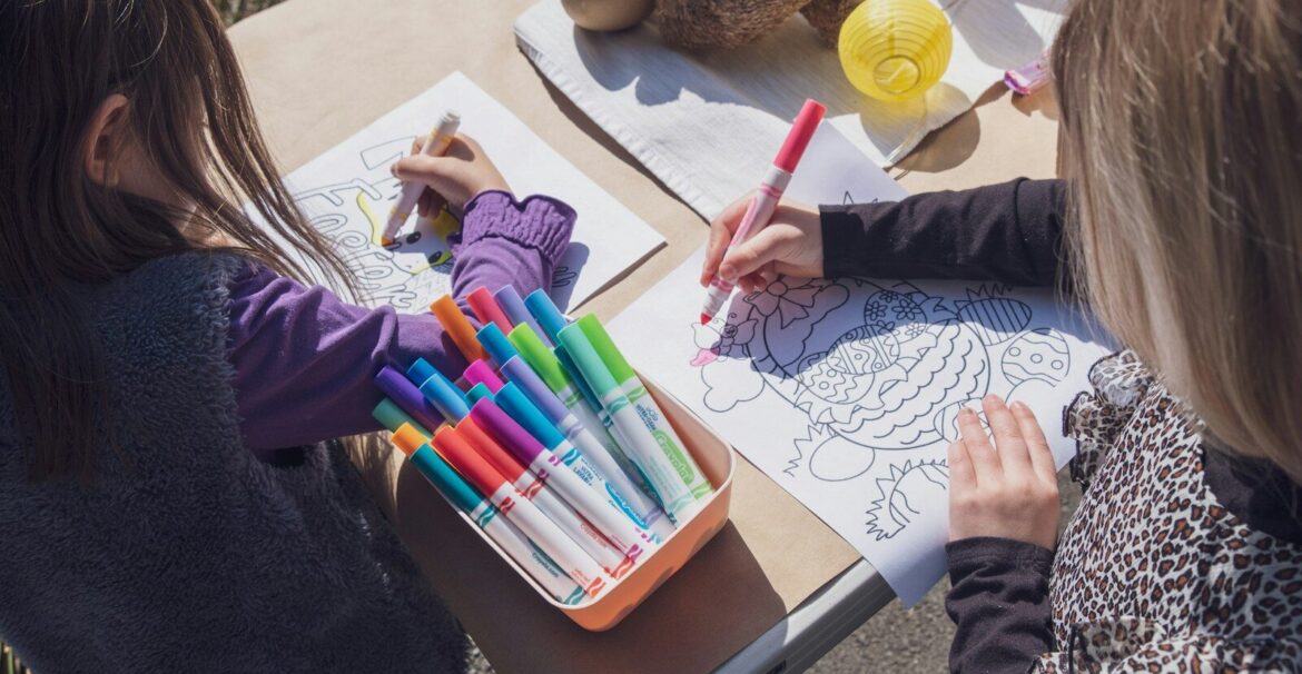 two young girls sitting at a table with markers and crayons
