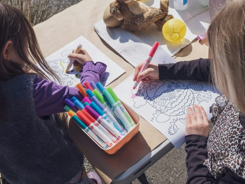 two young girls sitting at a table with markers and crayons