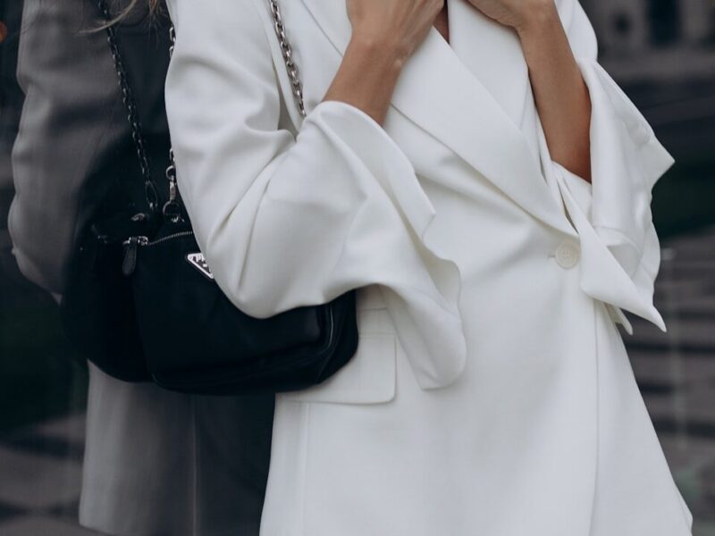 a woman wearing a white suit and holding a black purse