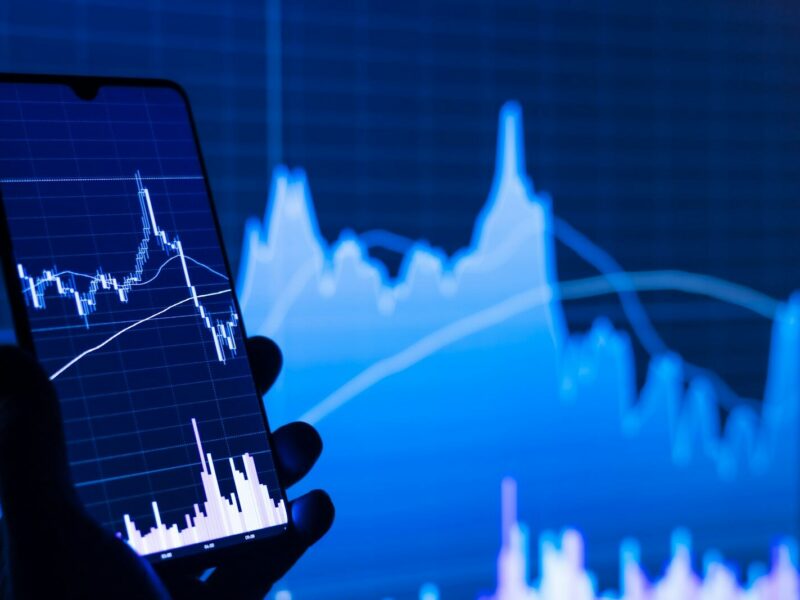 a person holding a cell phone in front of a stock chart