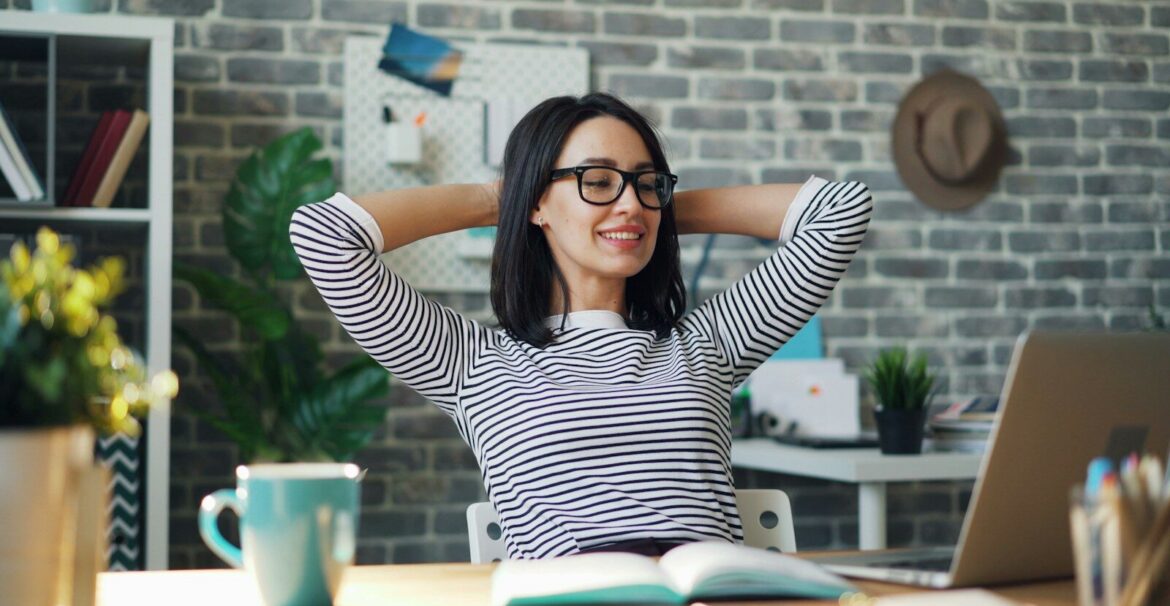 a woman sitting at a desk with her hands behind her head