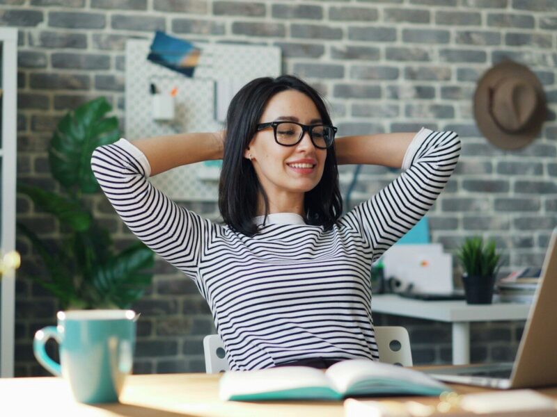 a woman sitting at a desk with her hands behind her head